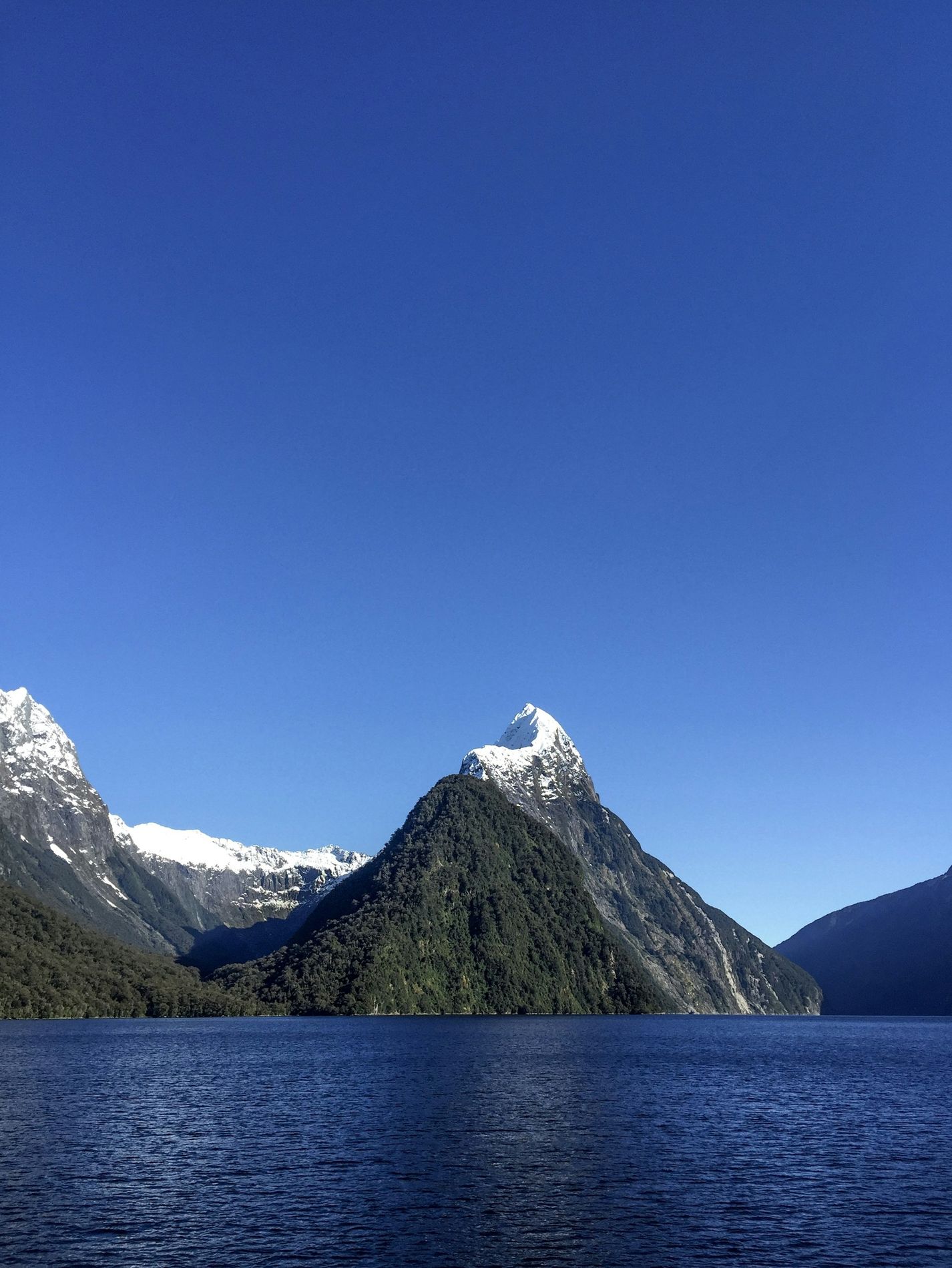 Mitre Peak, snow on its summit, against a deep blue sky
