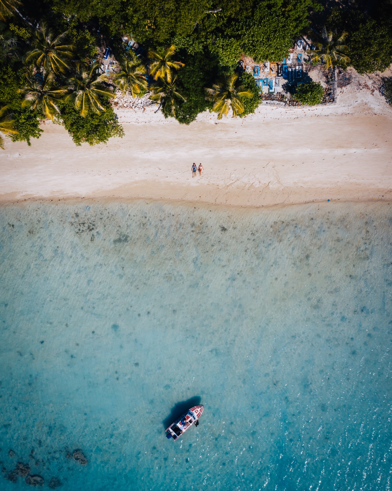 Aerial view of a white-sand beach and palms, a small boat on turquoise water