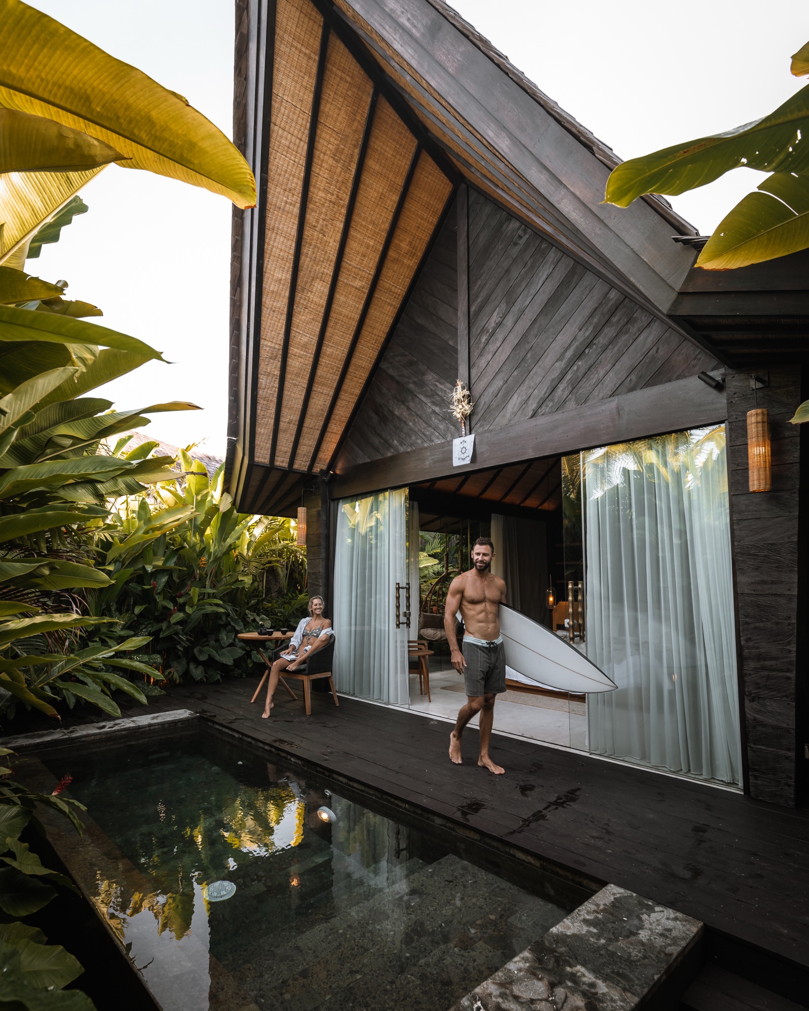 A guest carrying a surfboard past a private plunge pool at a villa in the jungle