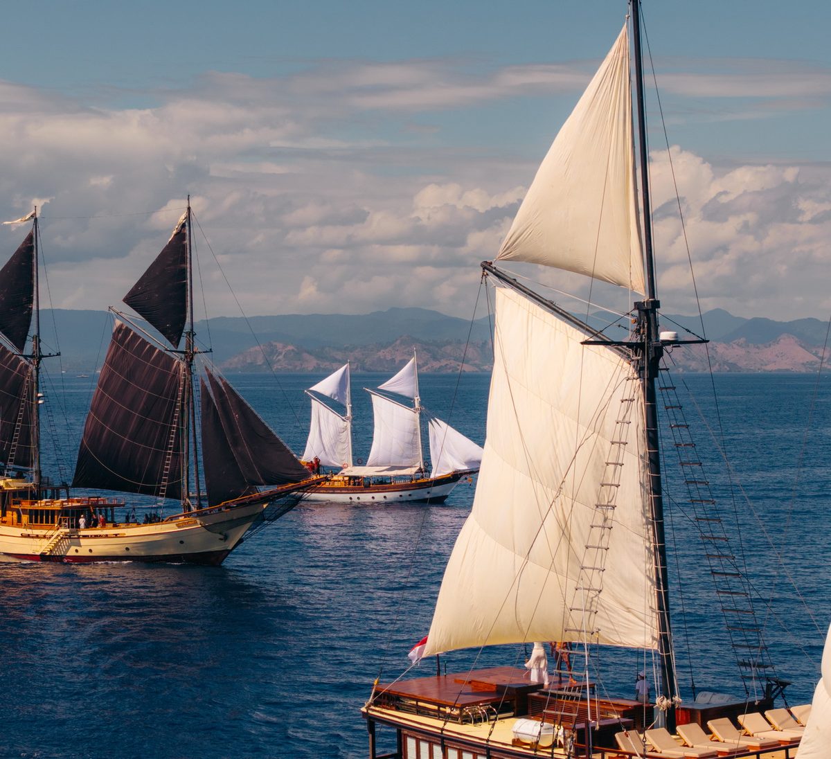 Two phinisi under full sail on a bright sea