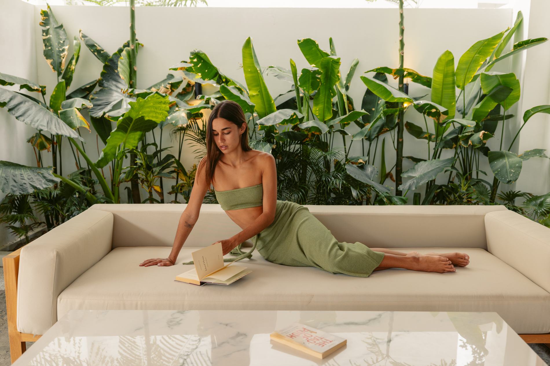 A woman reading on a sofa among banana leaves