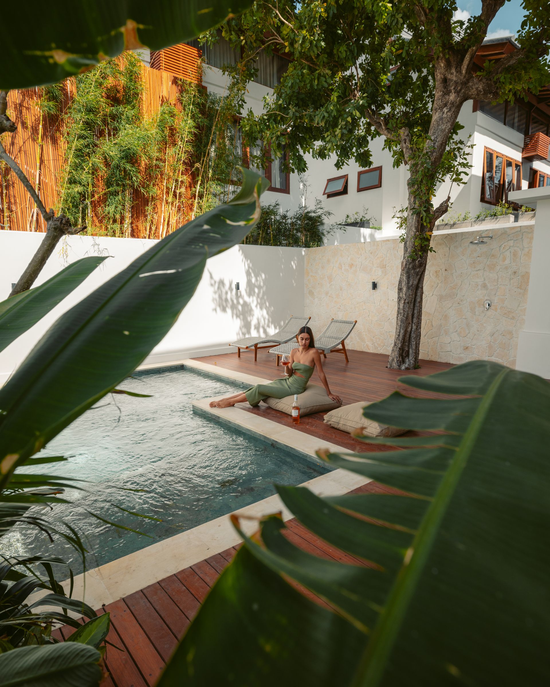 A woman resting beside a plunge pool on a timber deck, framed by large leaves