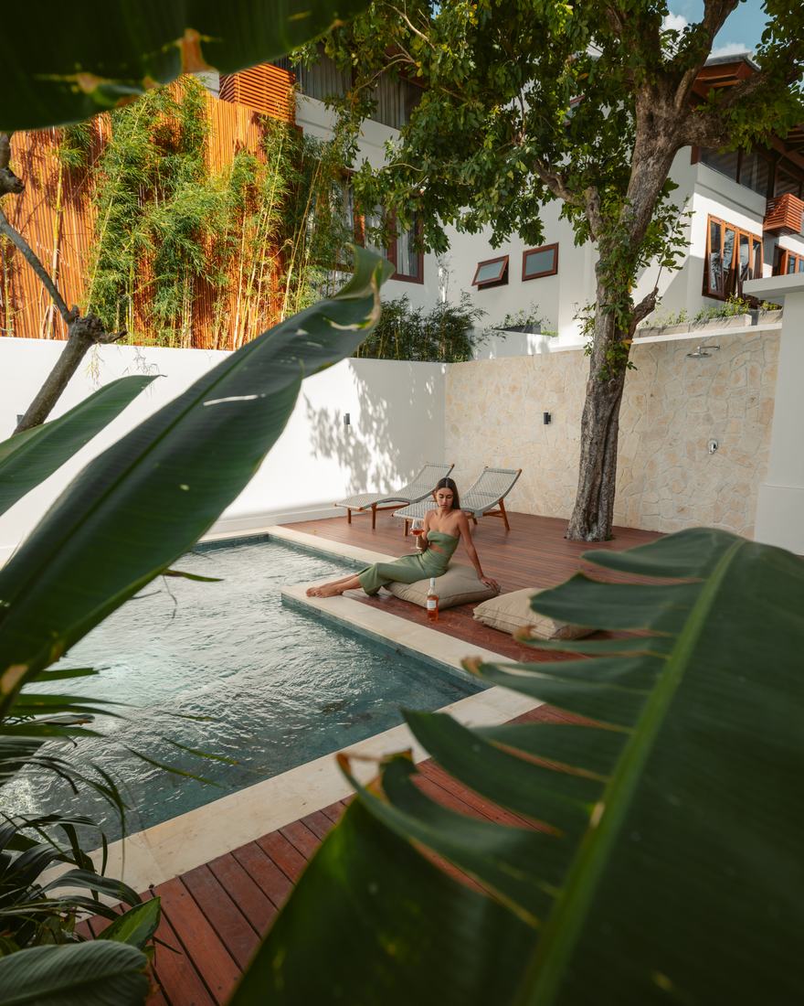 A woman resting beside a plunge pool on a timber deck, framed by large leaves