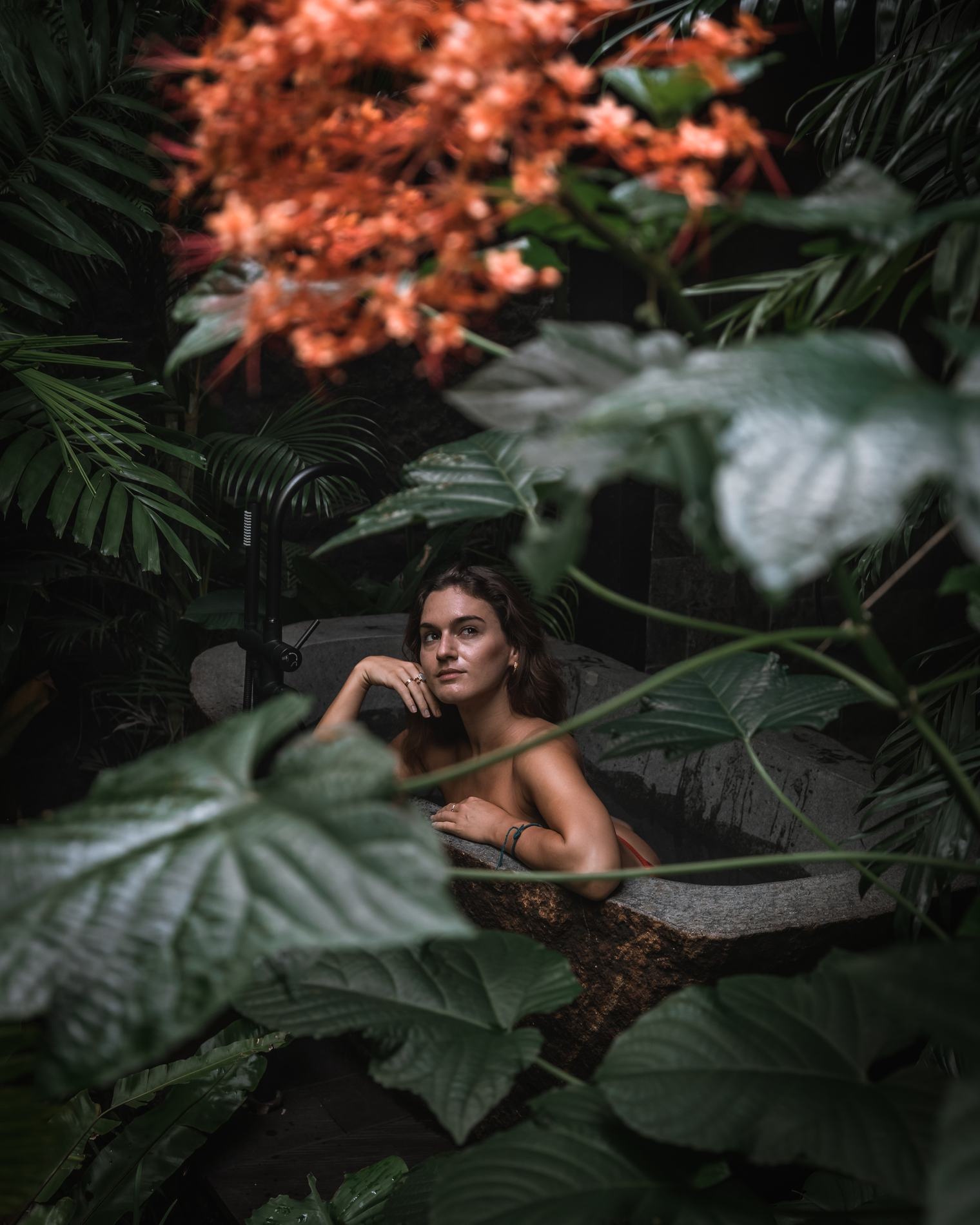 A woman resting her chin on her hand in a bath framed by leaves
