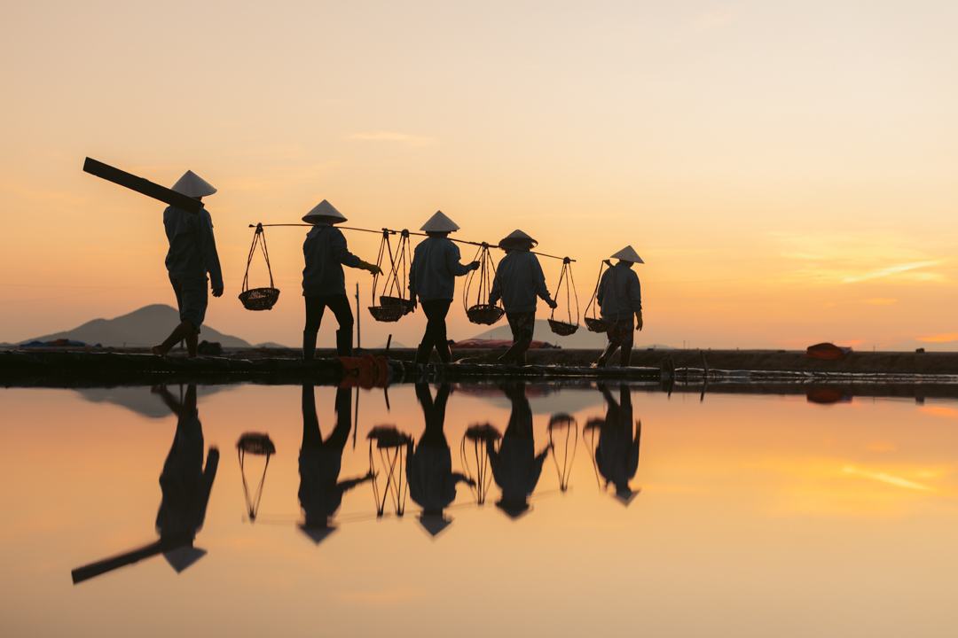Salt carriers silhouetted against an orange sky and its reflection