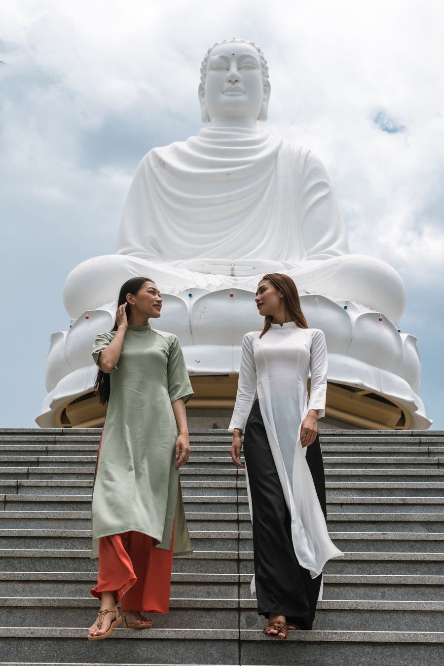 Two women in traditional dress walking down steps below a large white Buddha