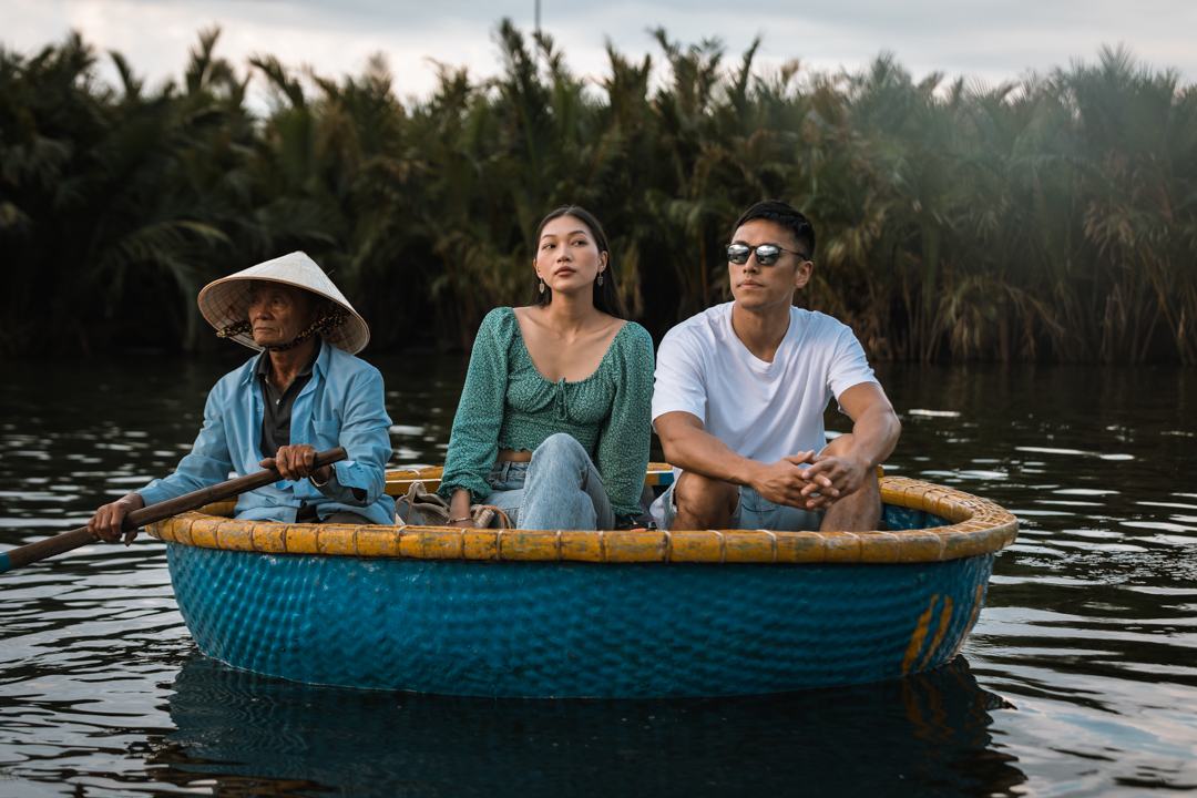 A couple riding in a round basket boat with a rower in a conical hat