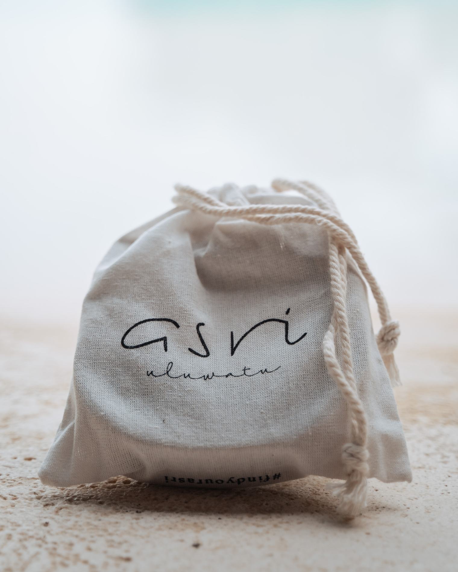 A cotton pouch printed with the Asri name on pale sand