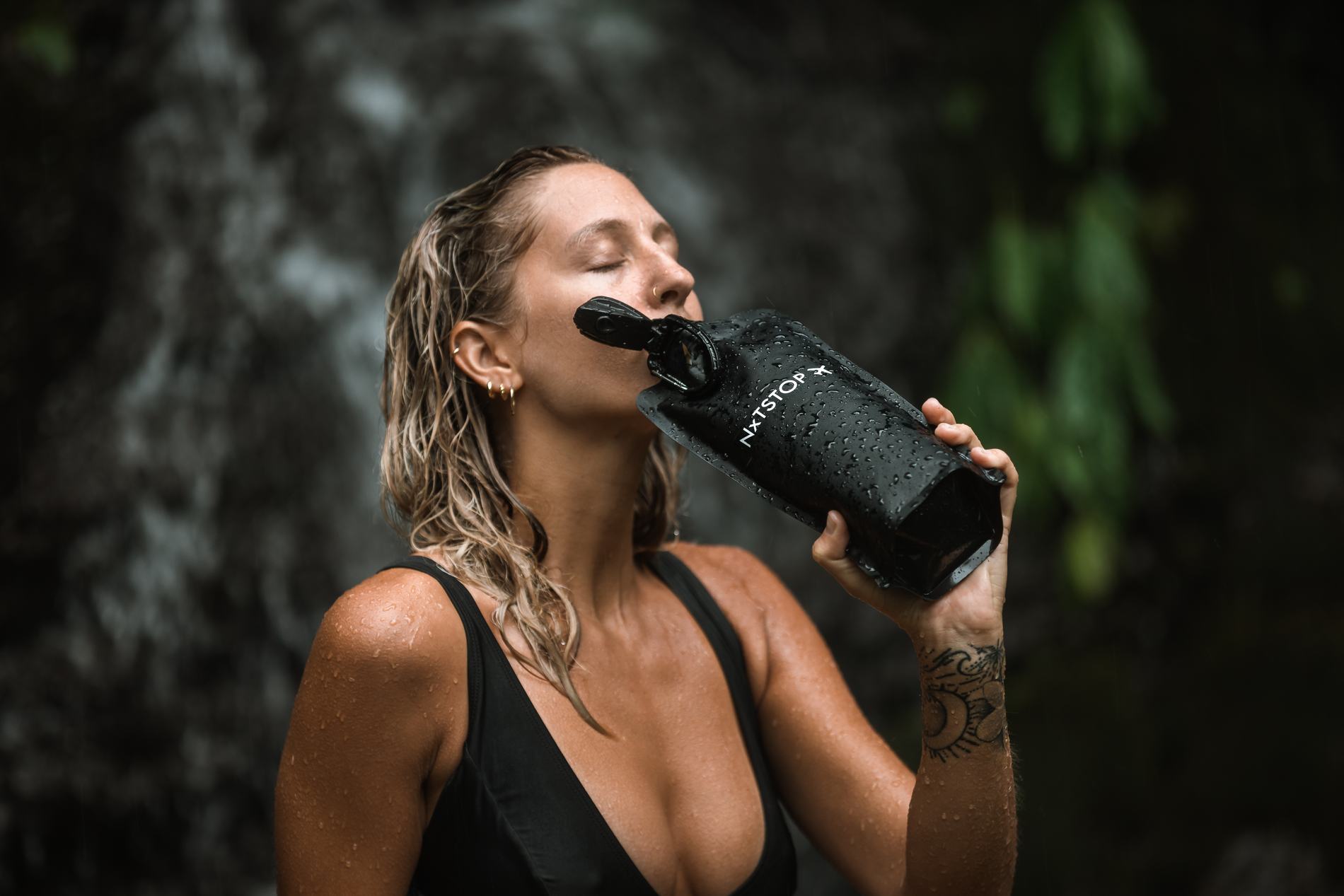 A woman drinking from the bottle, wet hair and eyes closed