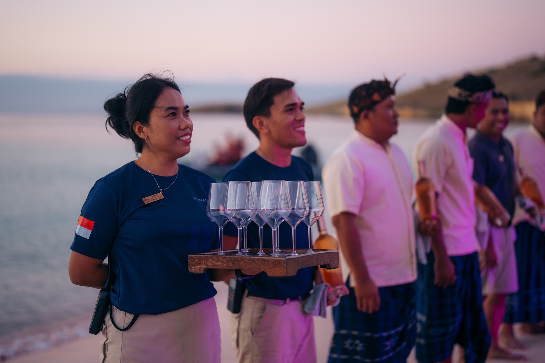 Staff carrying a tray of glasses, with local guests in sarongs beside them