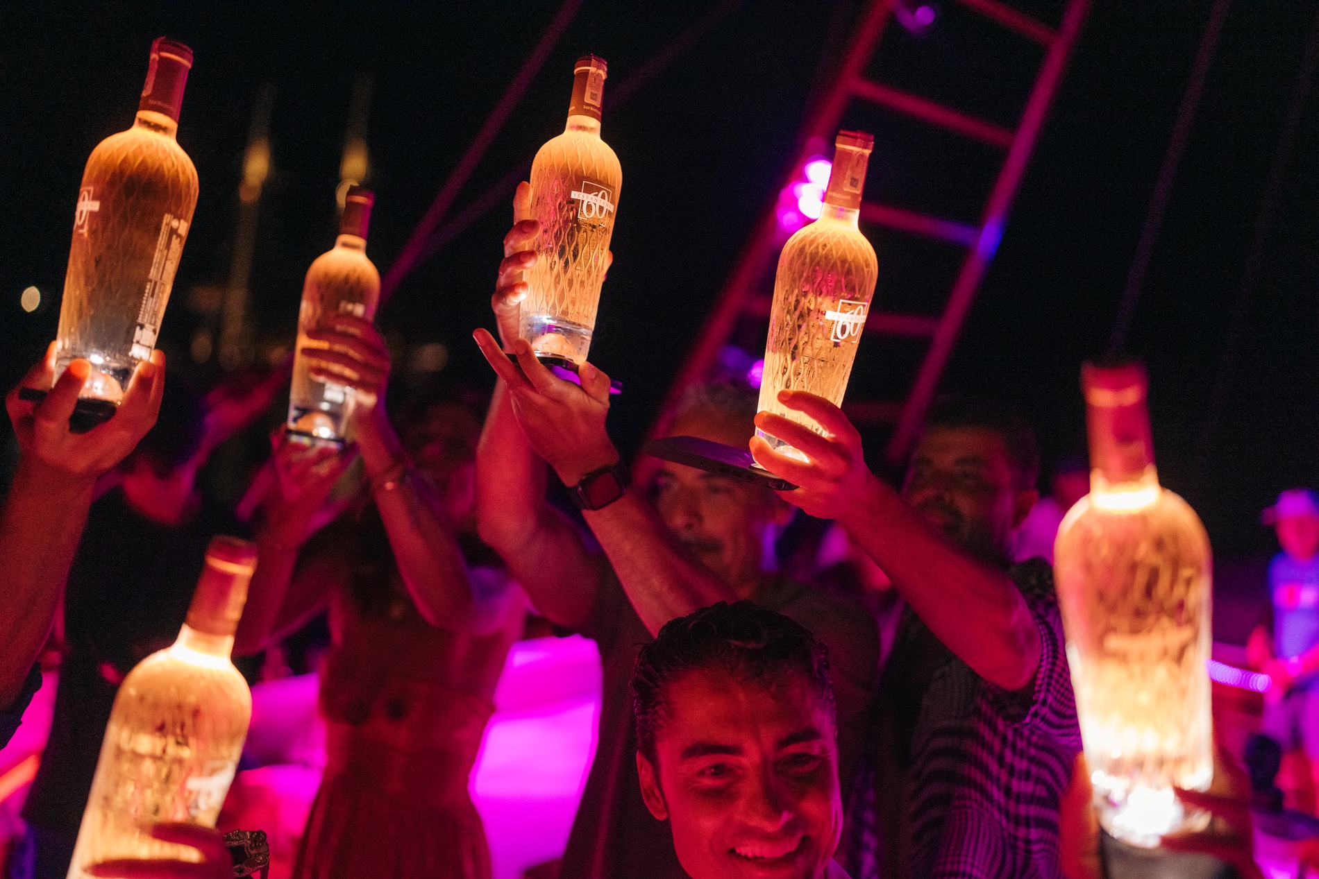 Guests holding up lit bottles in magenta light