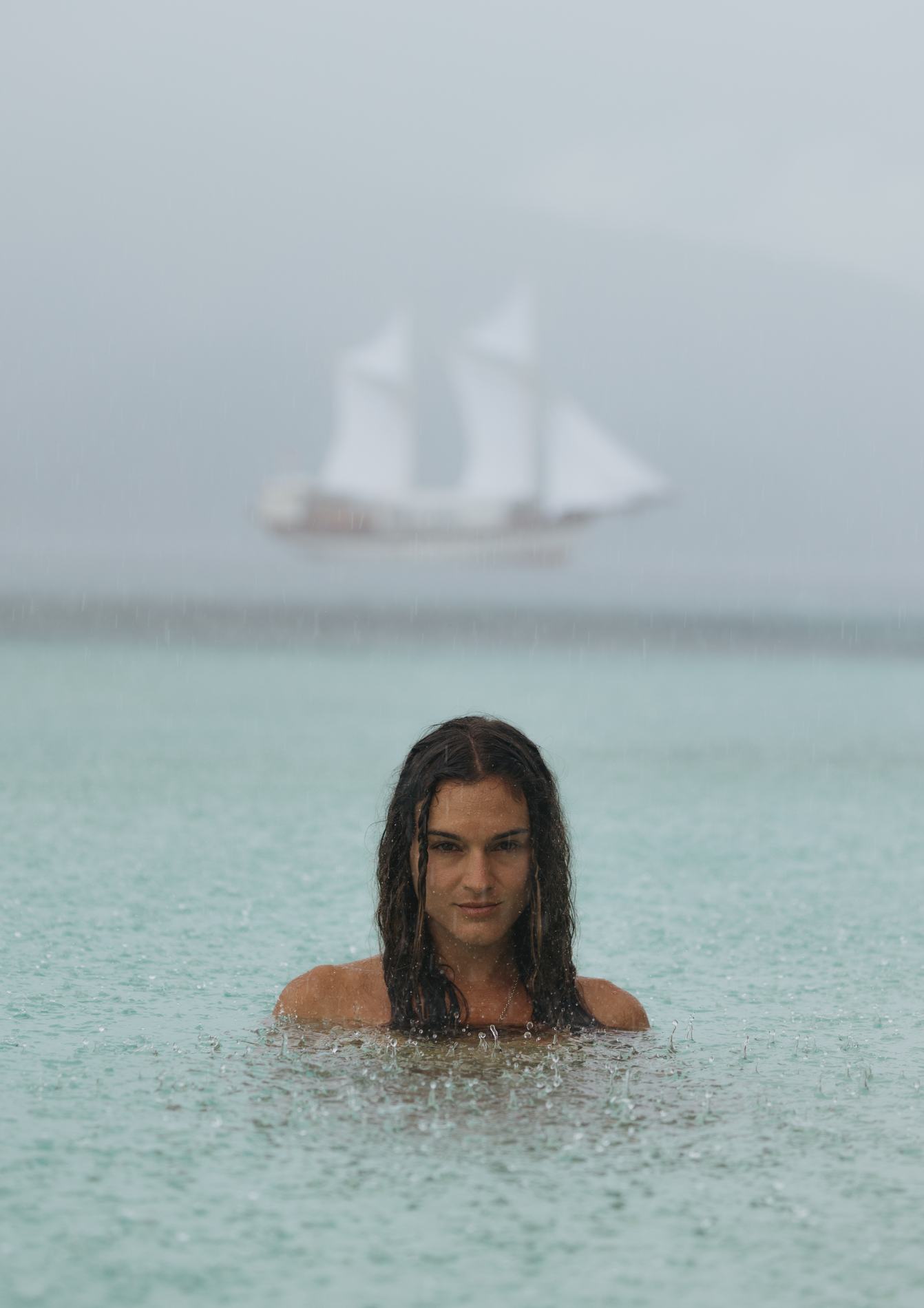 A woman standing in shallow water, the ship blurred behind her