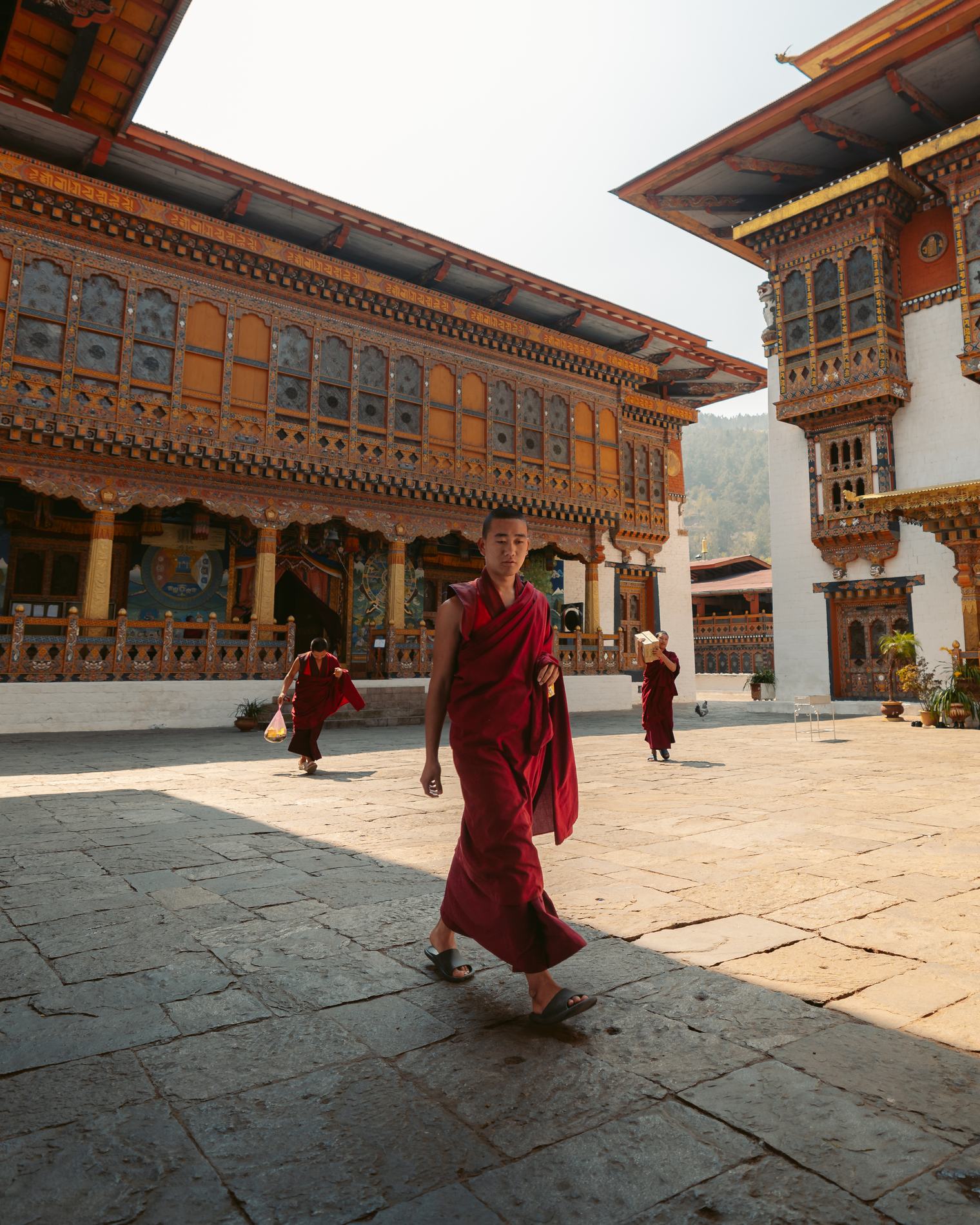 A monk crossing a sunlit stone courtyard