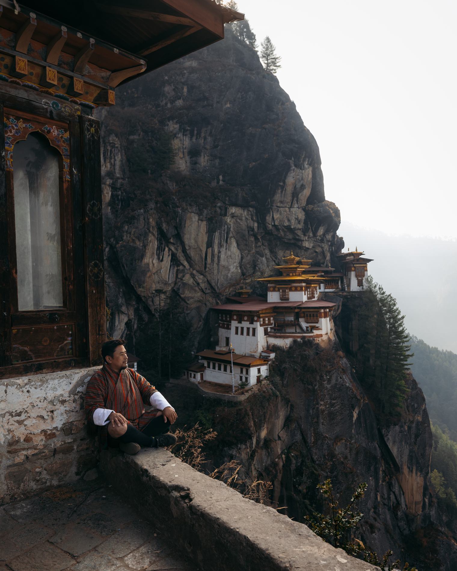 A man resting on a ledge below a monastery built into the cliff