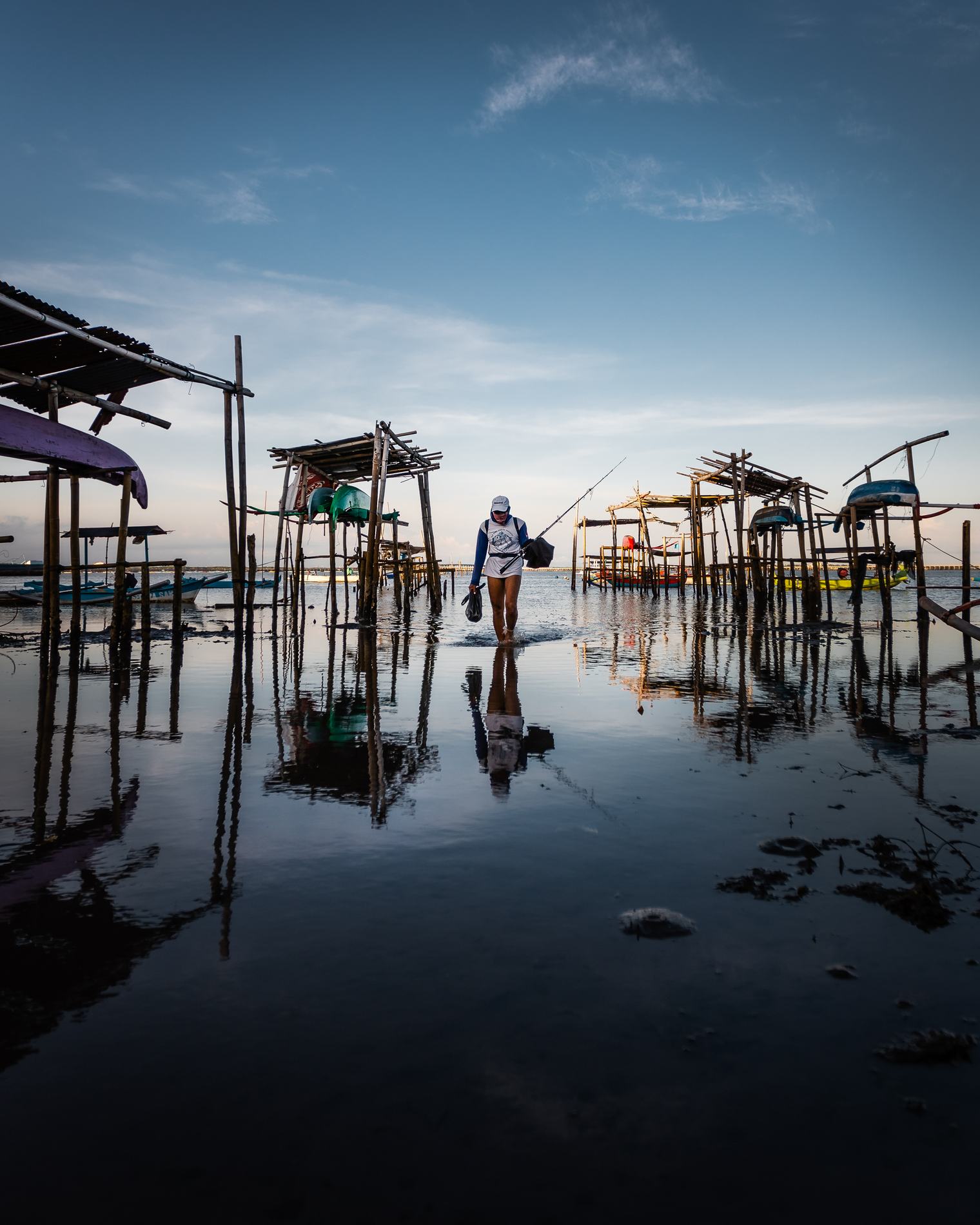 A fisherman wading through still water between wooden stilts