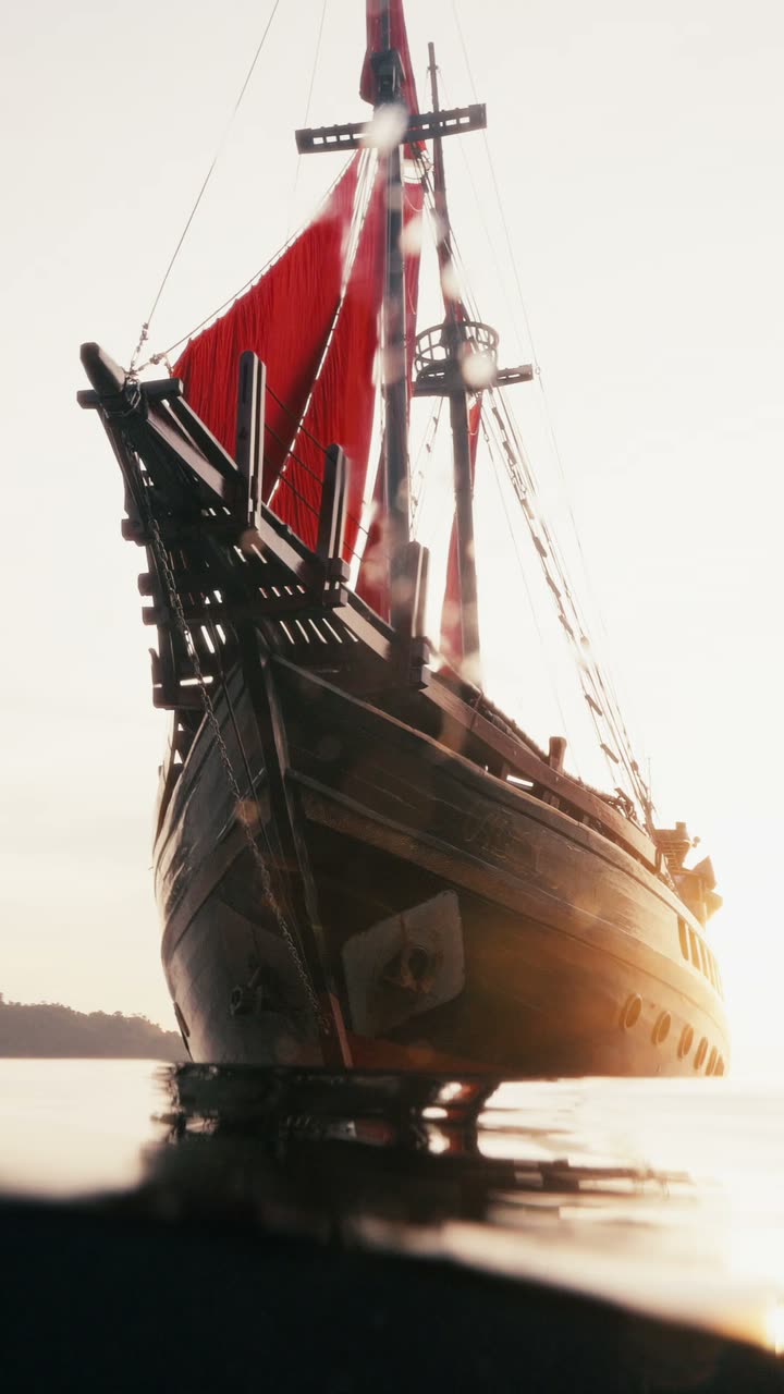 The ship under red sails on calm water, mountains behind